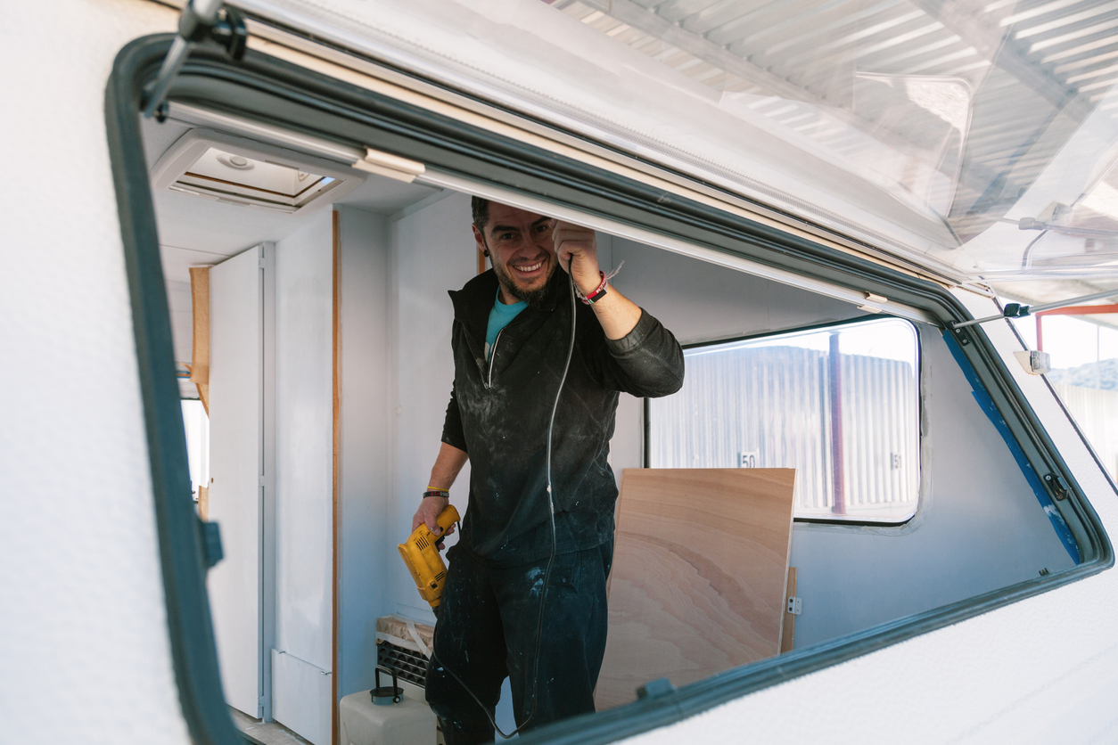 Young smiling man with a drill restoring his old caravan